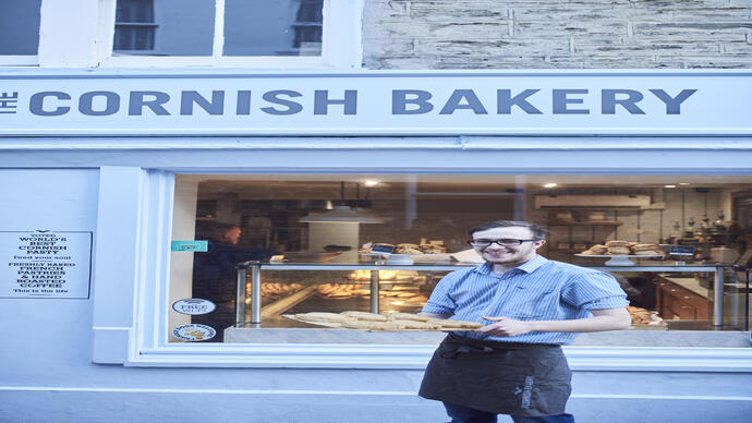 Un hombre sosteniendo una bandeja de empanadas de Cornualles fuera de una panadería