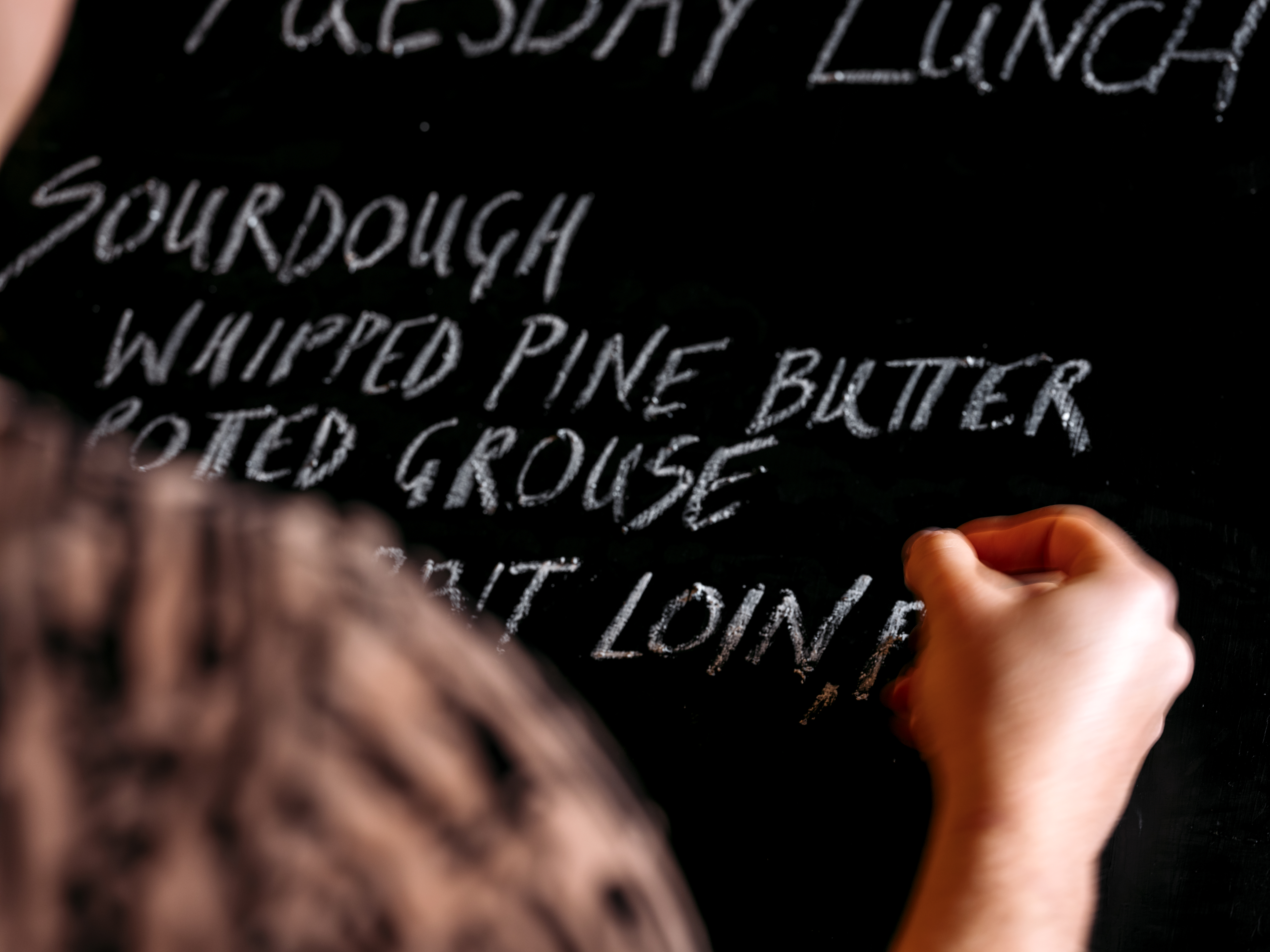 Close up of human hand writing menu on blackboard