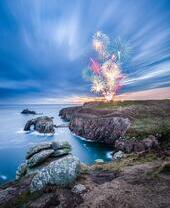 Firework display seen from across a rocky headland at twilight
