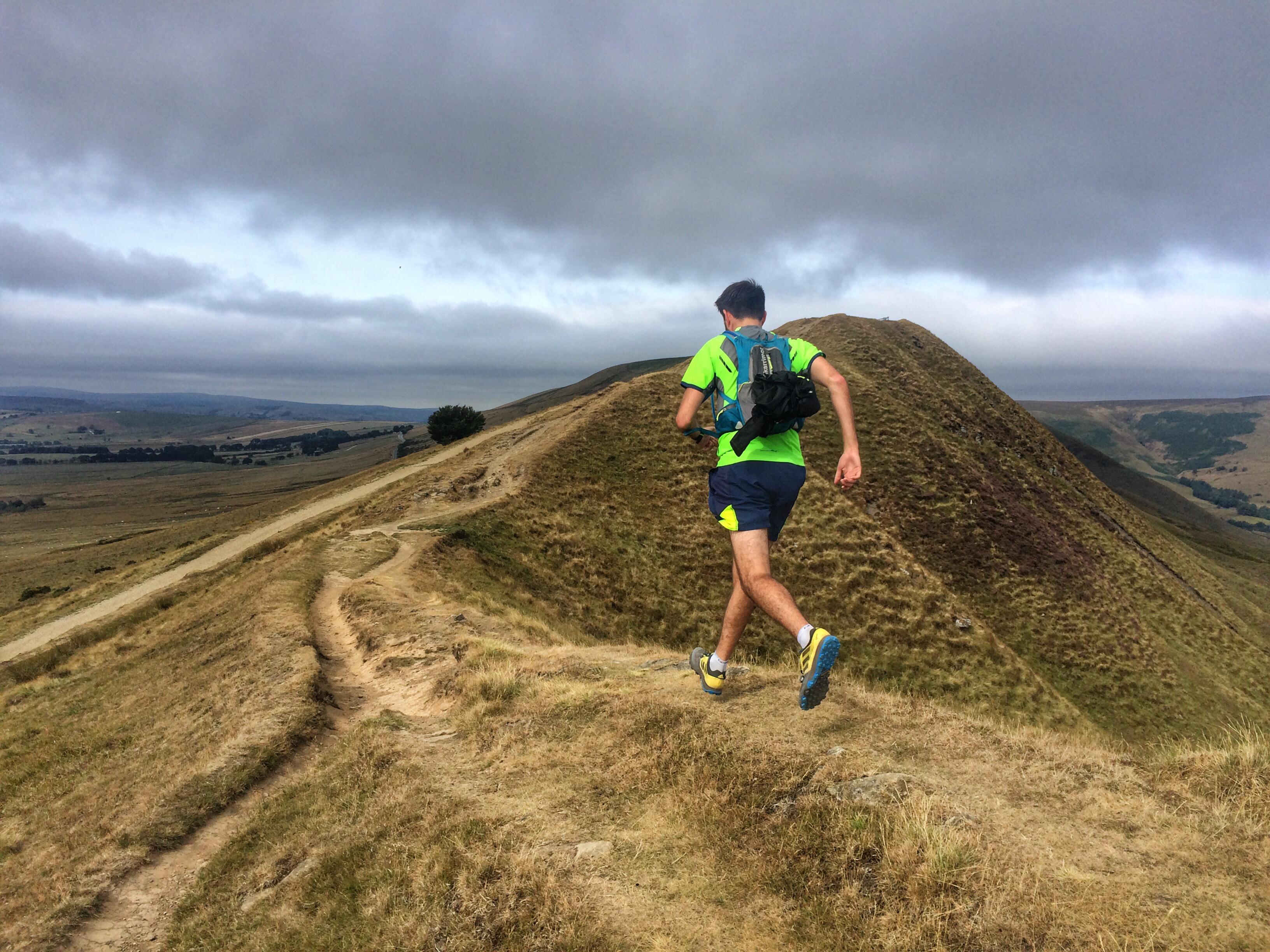 Trail runner running along a trail at the top of a steep hill