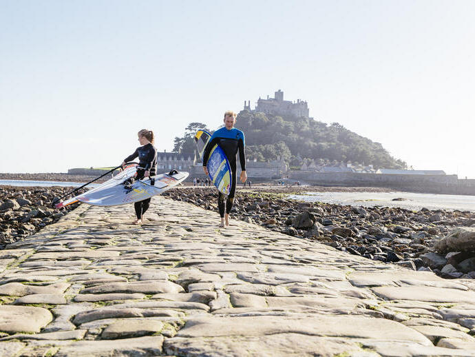 Windsurfers walking on a stone causeway that links an island to the mainland