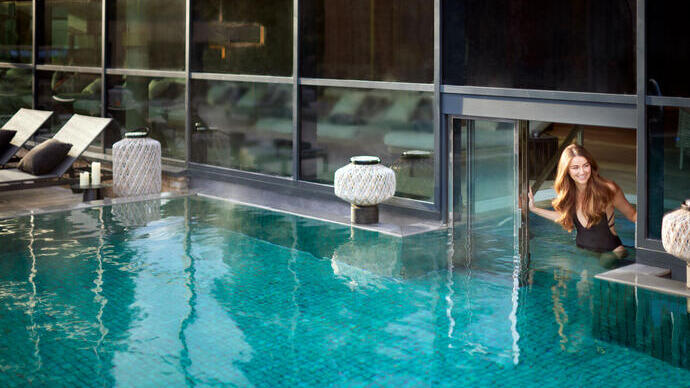 Modern pool beside large windows, lounge chairs, and decorative lanterns, with a person entering from indoors, creating a relaxing atmosphere.