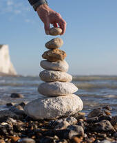 A hand posing with a stack of stones on the coast with white cliffs in the background