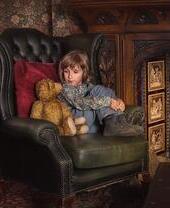 Young child sat on a green armchair in front of a fireplace with a teddy bear next to them at Criag y Nos Castle in the Brecon Beacons
