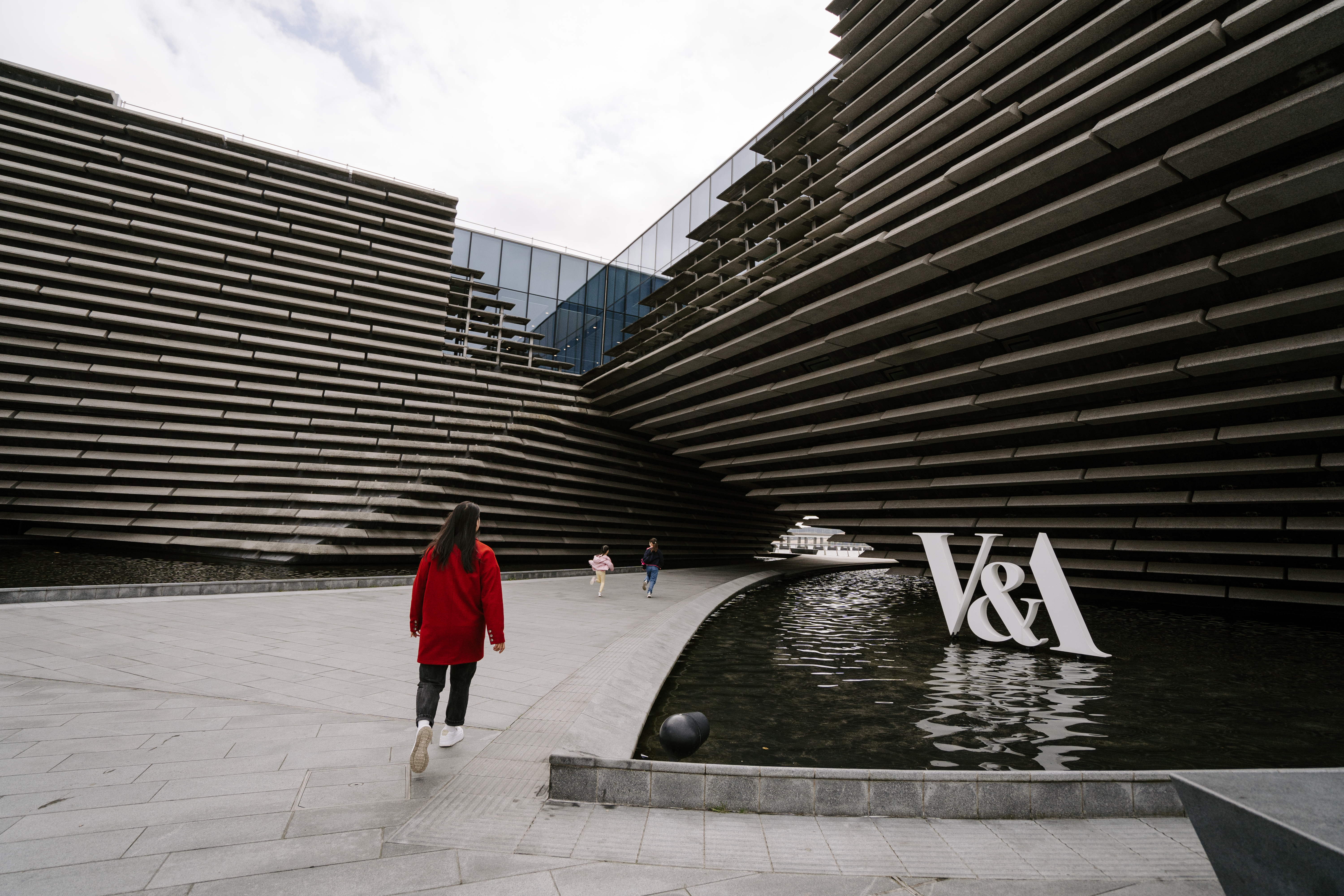 A woman and two girls walking by a modern museum.