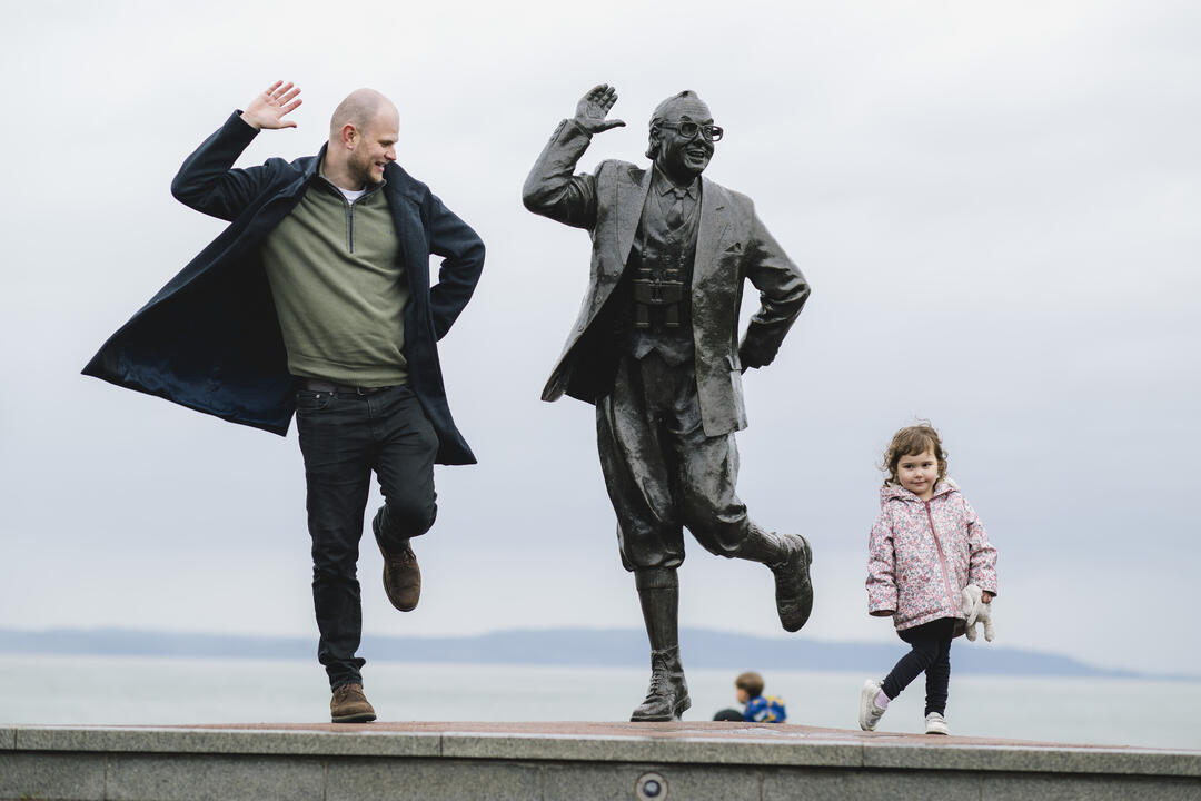 View of man, female child and statue of a man in front of the sea