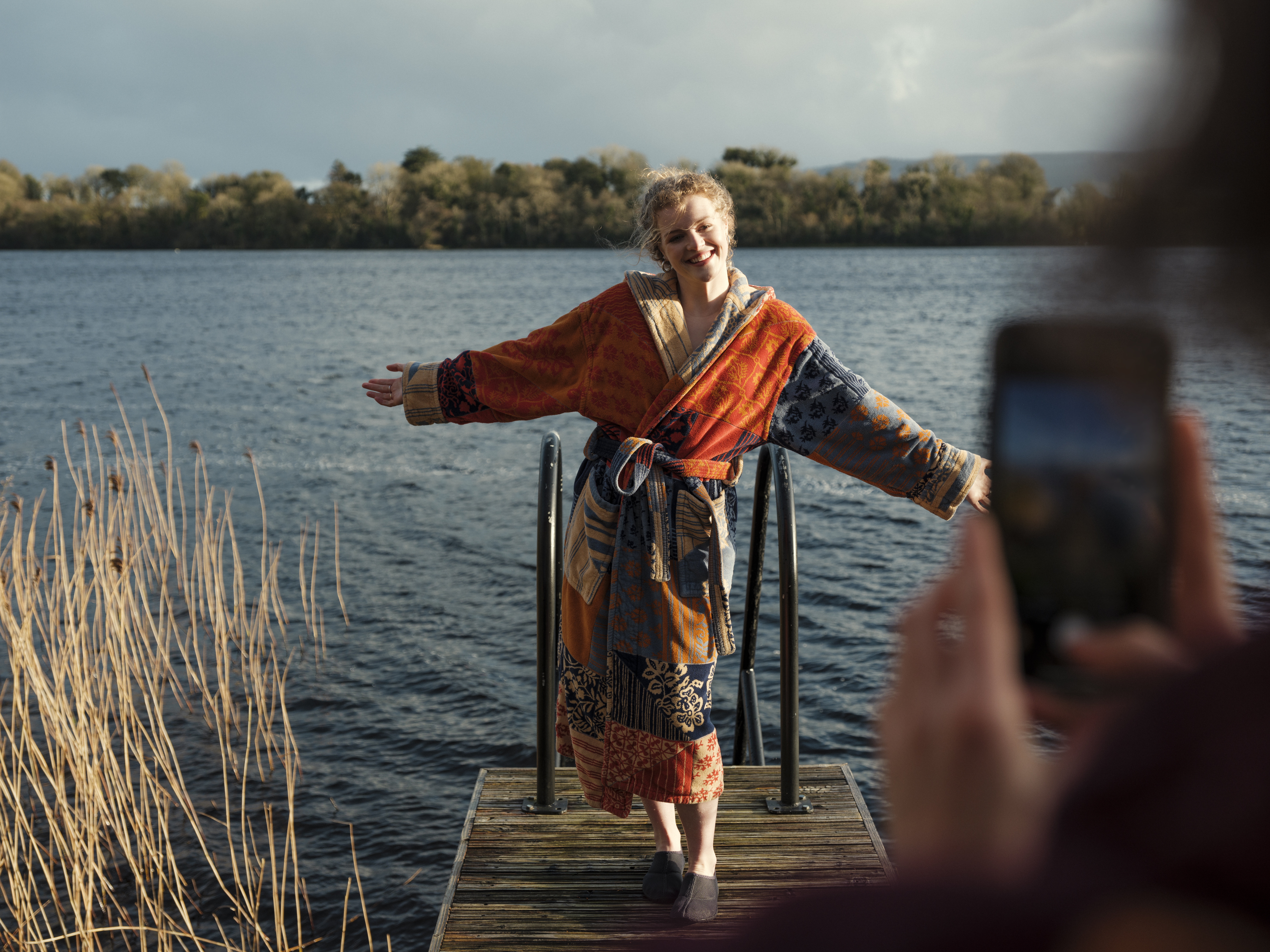 Mujer en albornoz posando para una fotografía frente al lago en Elements Spa Trail, Finn Lough