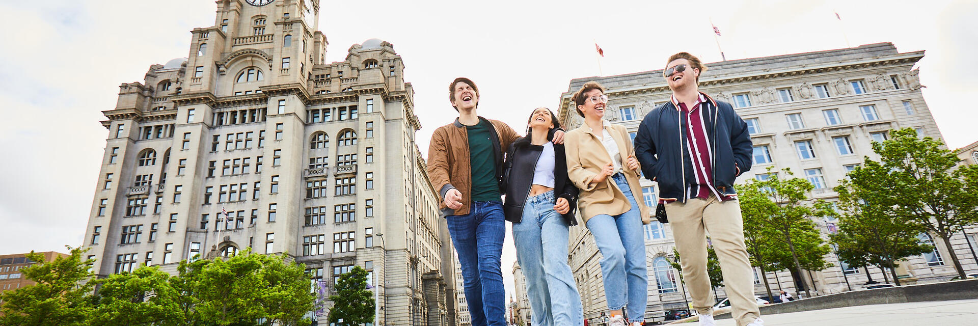 Four friends exploring a local city walking along waterfront promenade, with historic buildings in the background