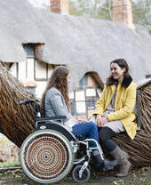 Mujer en silla de ruedas y amiga sentadas en un banco de mimbre esculpido