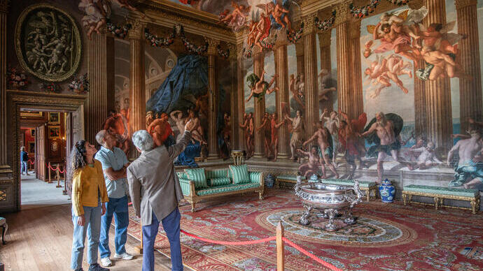 A man and a woman with a tour guide in an ornate room with paintings