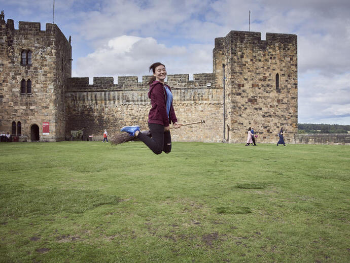 Young woman hovering on a broomstick in the Outer Bailey of Alnwick Castle
