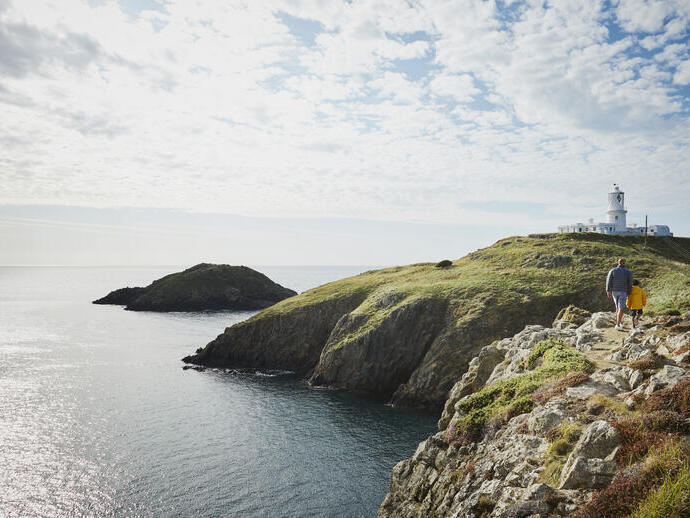 Un homme et un enfant marchant sur un sentier côtier en direction d'un phare