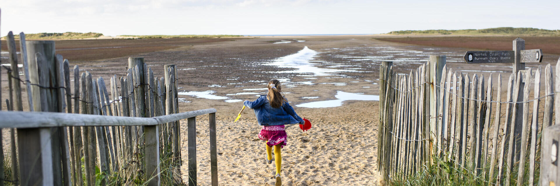 Una niña corriendo por un sendero hacia la playa de Holkham