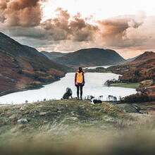 Woman standing with two dogs looking down at a lake in a valley