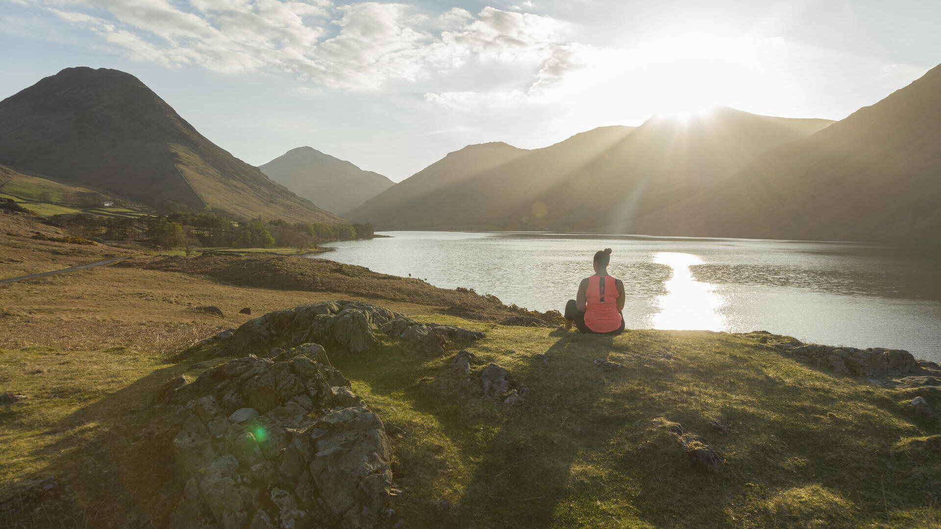 Woman, meditating in green valleys, near lake. The sun is shining.