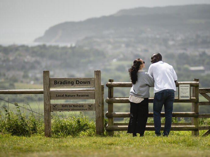 A man and a woman stand at gate with the town and sea beyond