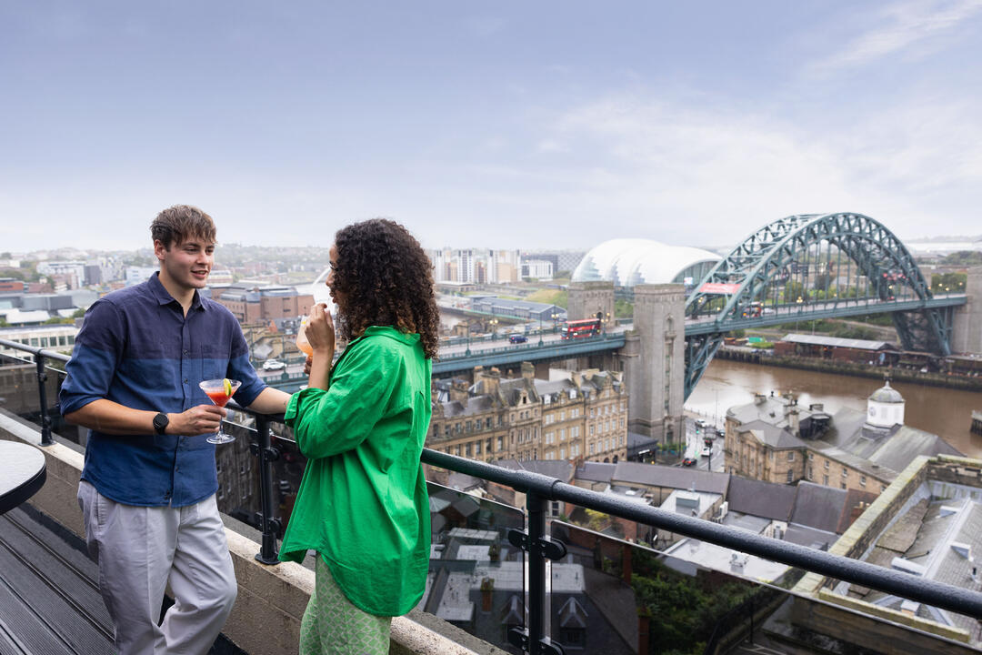 Paar genießt einen Cocktail im Above, einer Bar mit Blick auf einen Fluss und eine Brücke in einer Stadt