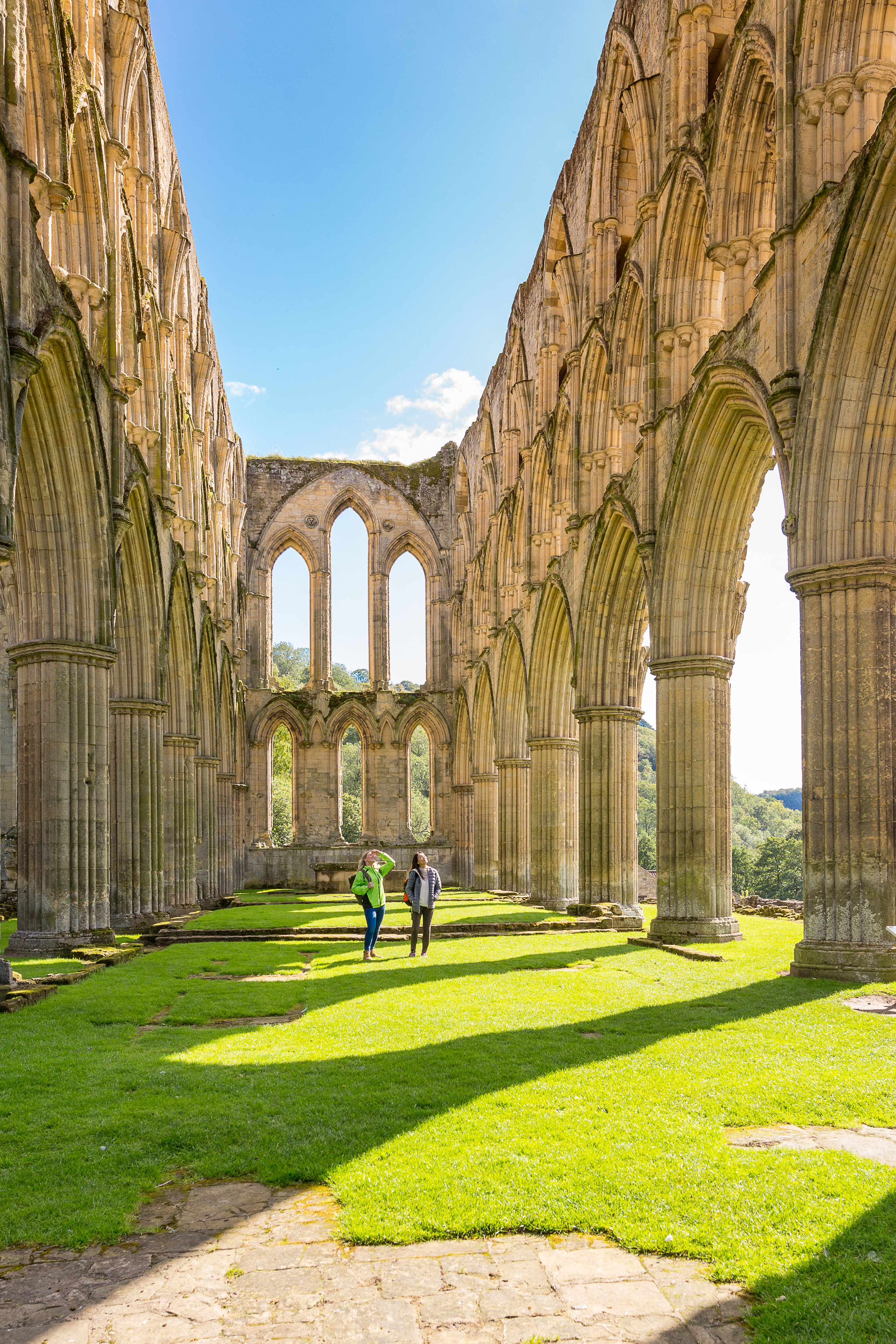 Two people walking between outdoor stone pillars of a ruined building