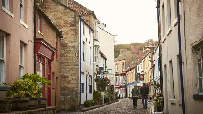 Two people walking down a cobbled village lane