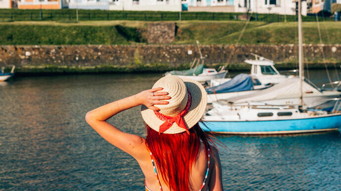 Femme assise sur le mur d'un port, regardant les bateaux
