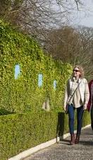 Two women walking along an hedge in a park