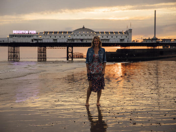 Donna in piedi sulla spiaggia vicino al molo al tramonto