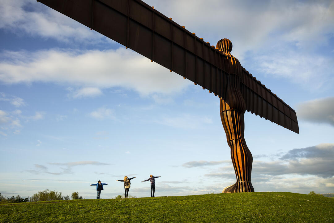 Three people posing near a giant steel sculpture