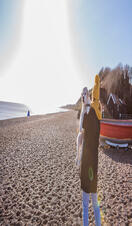 A woman carrying a dog along a beach in Dunwich