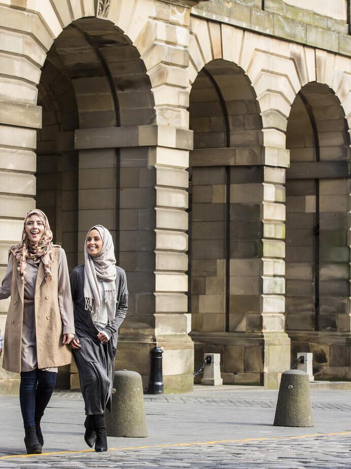 Tre donne che camminano sotto archi di pietra in una città