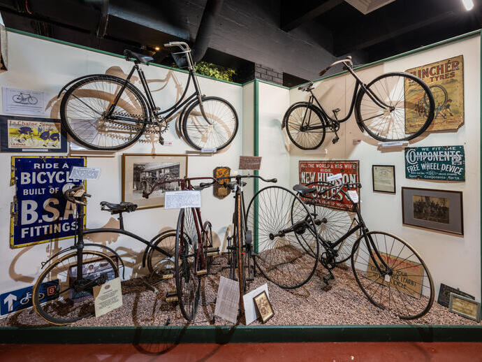 Exhibit of vintage bicycles, historical cycling posters, and antique cycling memorabilia displayed in a museum setting.