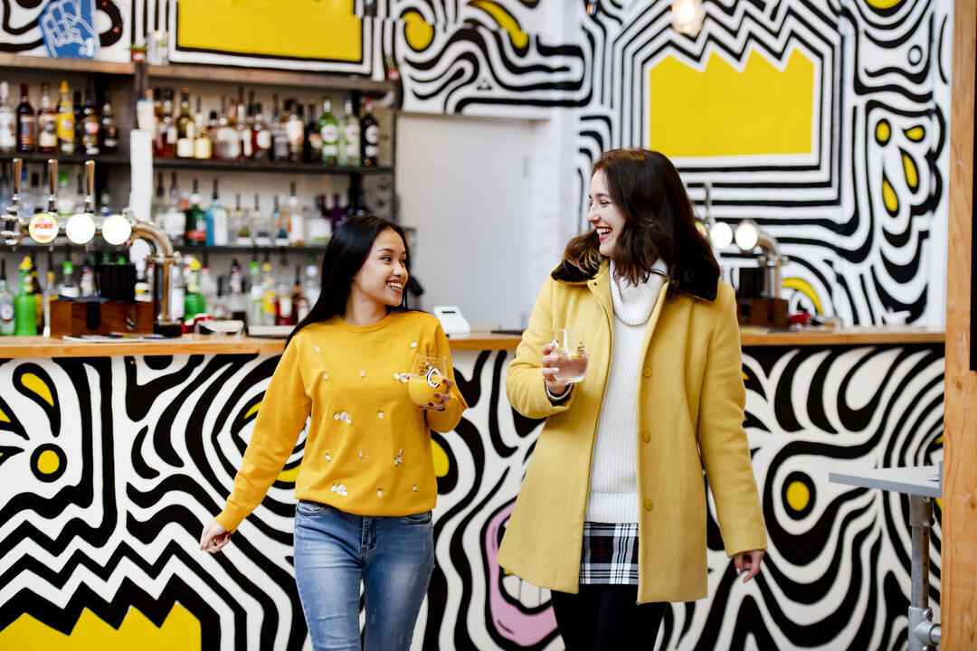 Deux femmes tenant des boissons et s'éloignant d'un bar