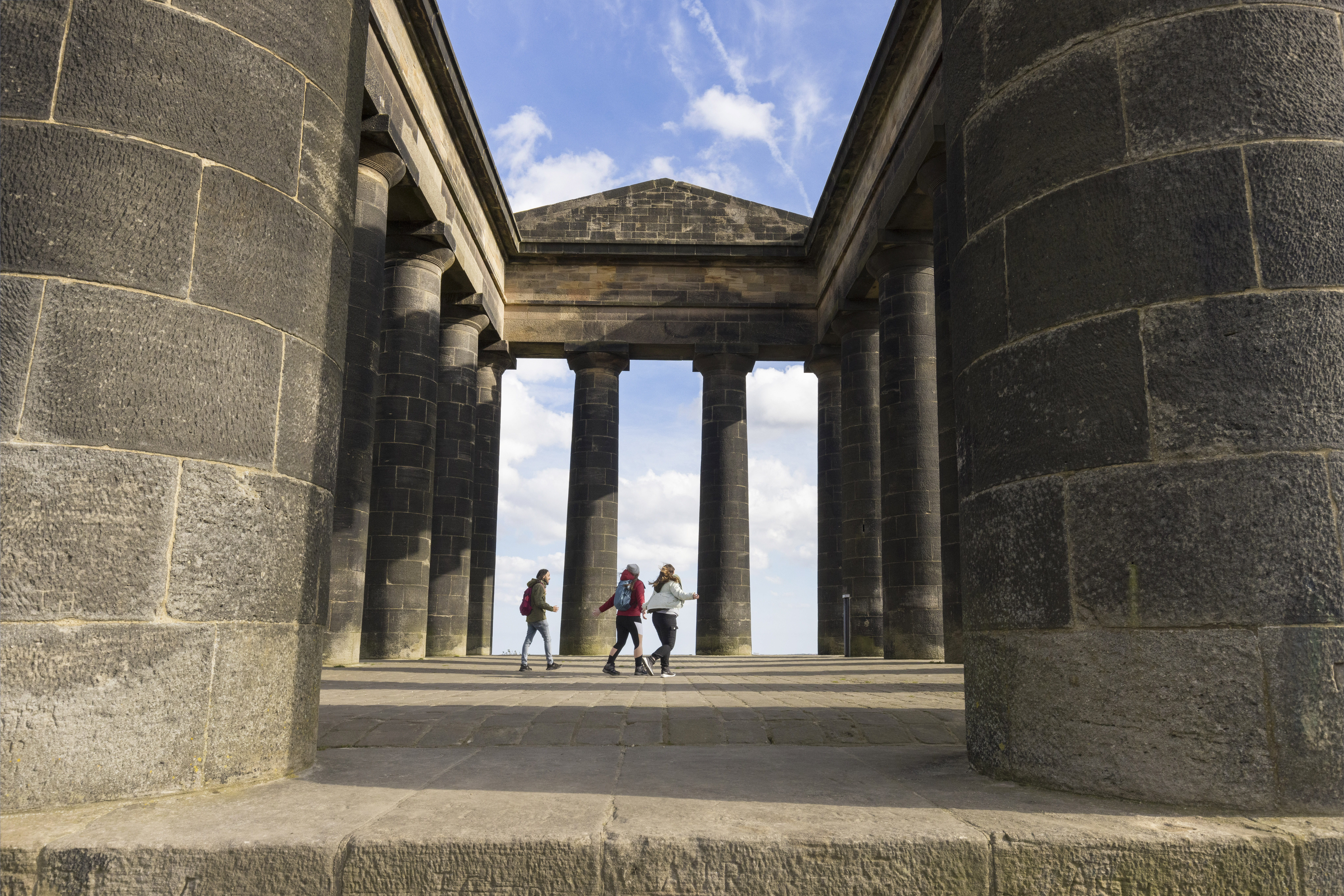 Three people exploring an antique stone monument with large archways and pillars.