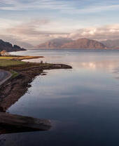 Una strada tortuosa e remota che costeggia un grande lago nelle Highlands scozzesi.