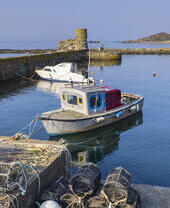 Deux petits bateaux amarrés dans un petit port en pierre par une journée ensoleillée, avec sept casiers à homards au premier plan.