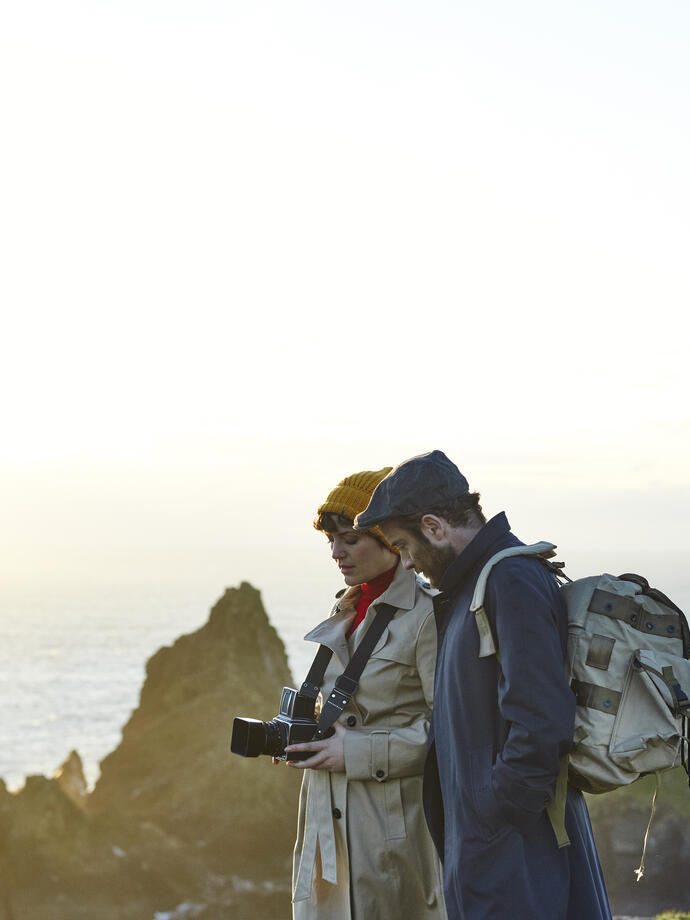 Couple debout au sommet des falaises, la femme tient un appareil photo et l'homme porte un sac à dos