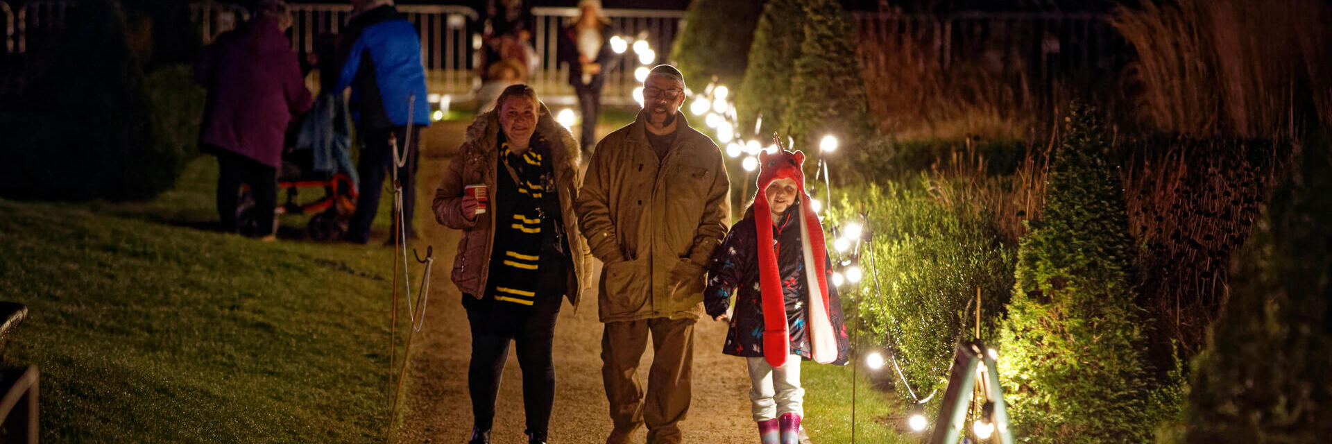 A family walking down a path lit up with fairy lights at night.