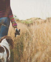 Woman and dog walking through tall wheatgrass.