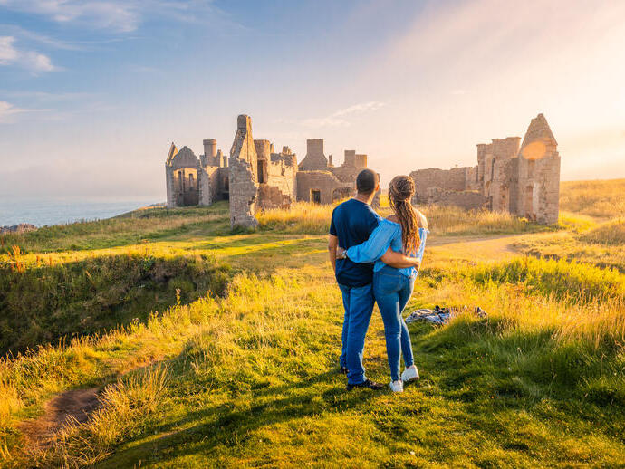 A couple enjoying the views of a castle remains at golden hour.