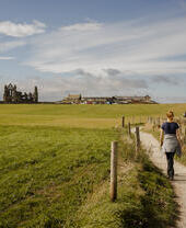 Woman walking along a coastal path towards a ruined abbey