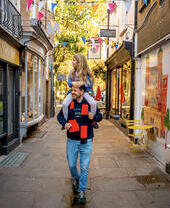 Man with a child on his shoulders walk through a pedestrian street with shops either side