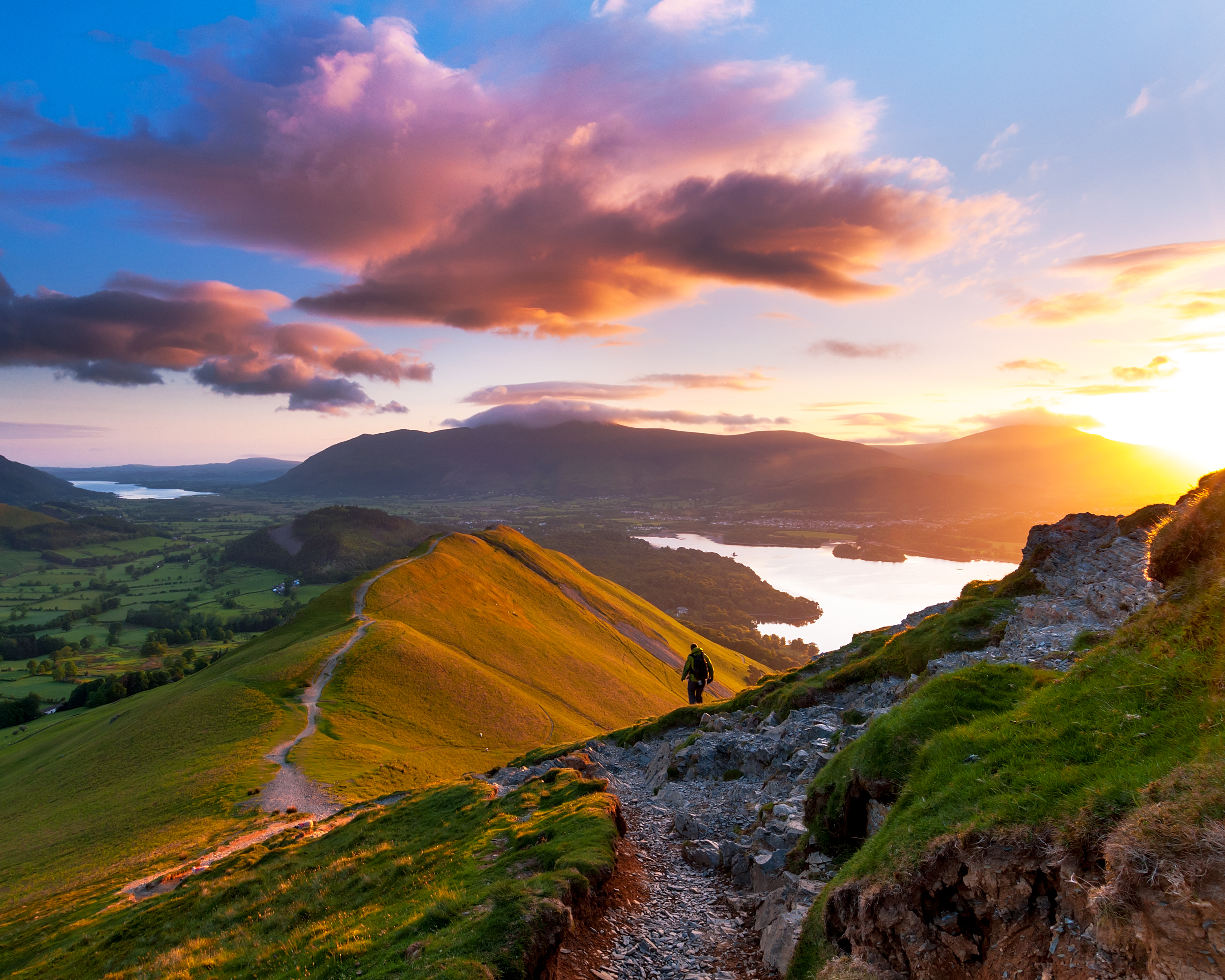 Hiker walking along a path on the mountain ridge at sunset