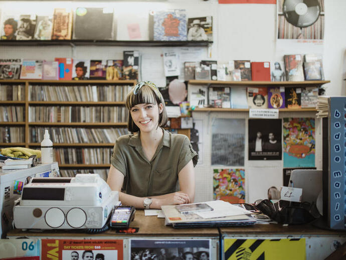 Young woman smiling, behind a counter in a record shop, with the till and card reader in front of her