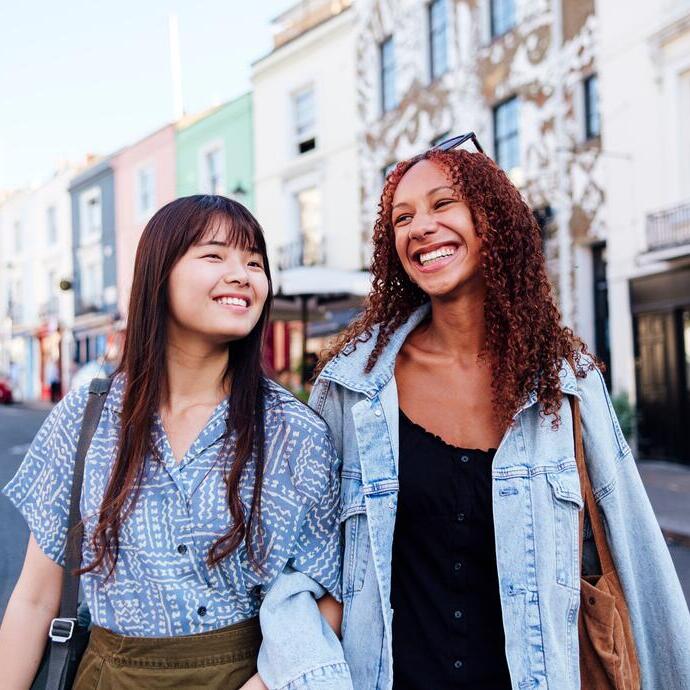 Deux jeunes femmes marchant bras dessus bras dessous dans une rue, souriantes