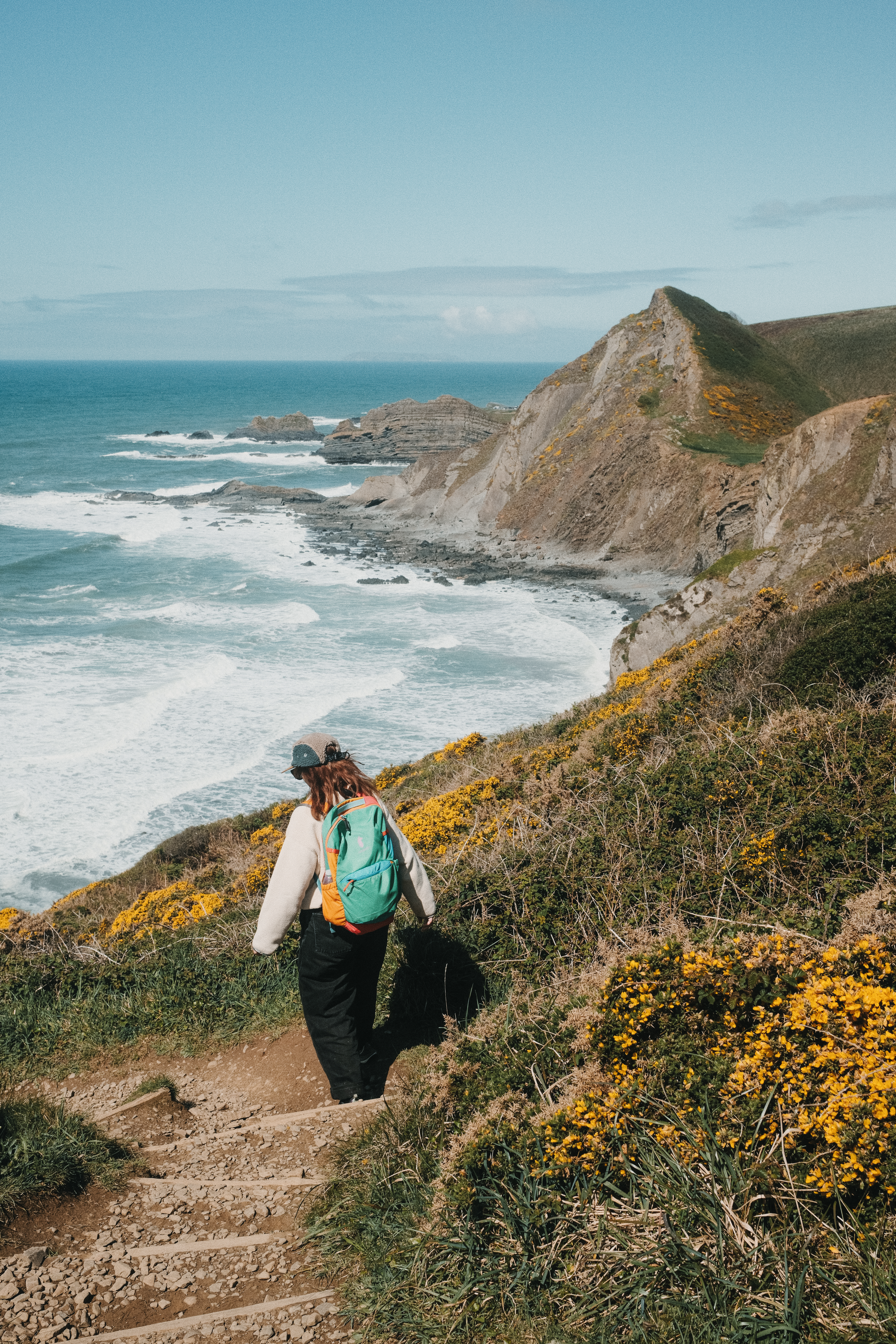 A woman walks along a coastal path with sea and headland in the distance