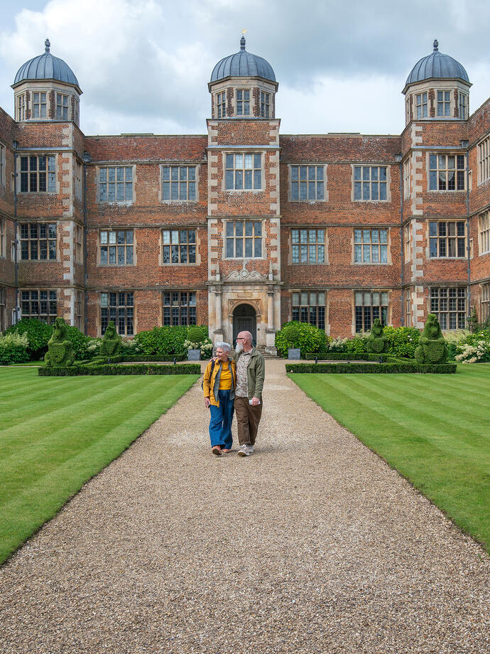 A man and a woman walking together along a path in front of a heritage building
