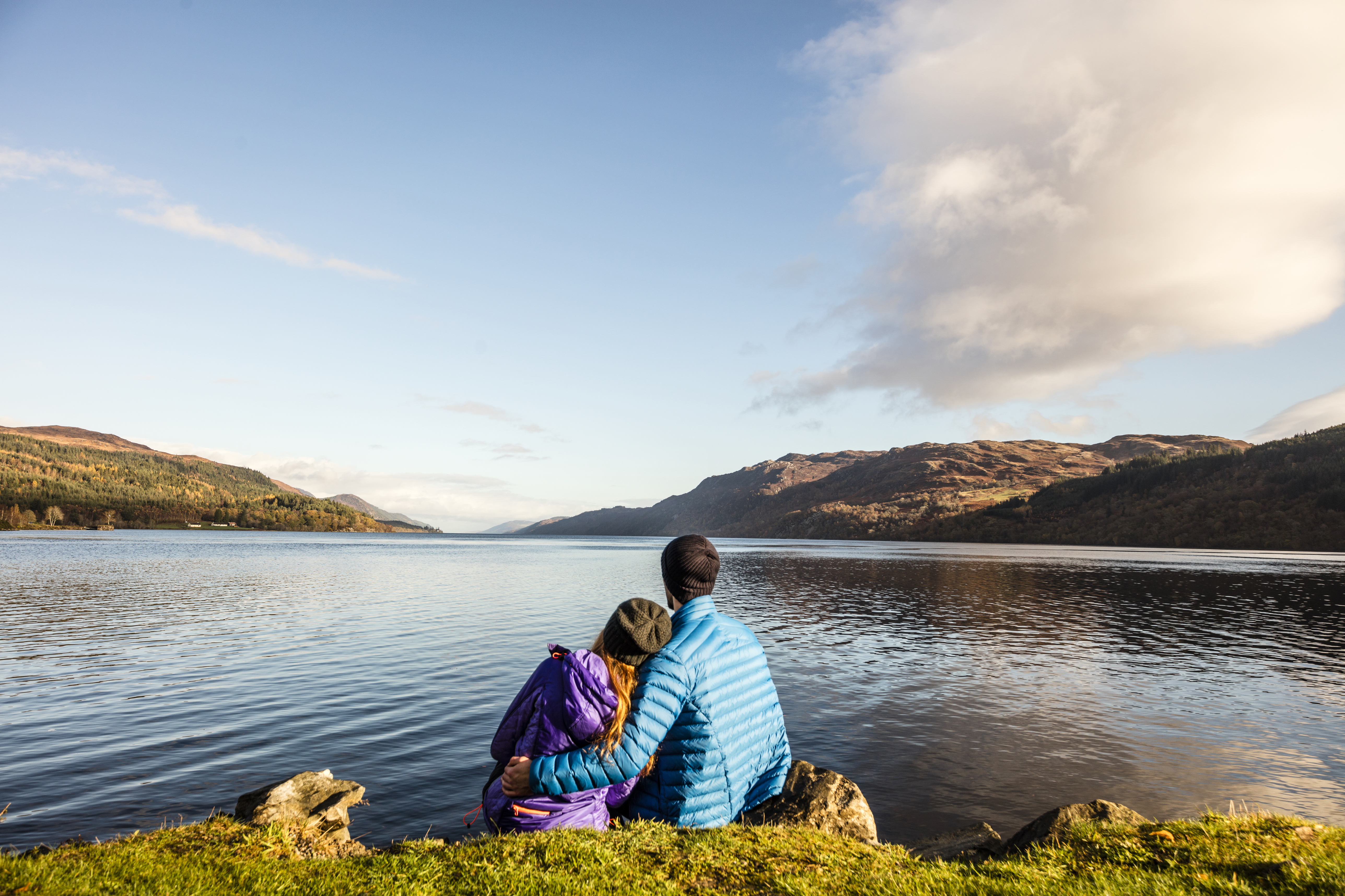 A man and woman sat looking across a lake