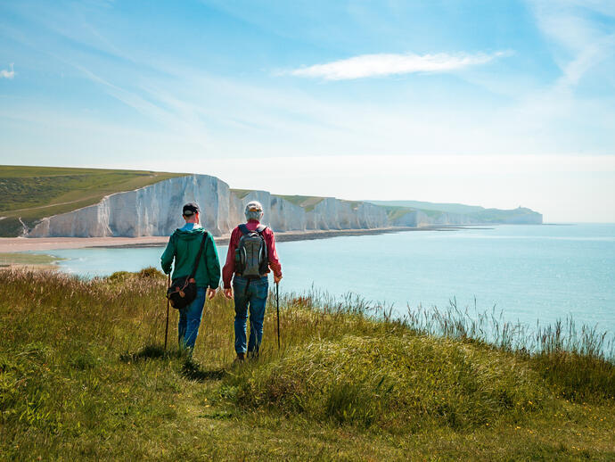 Two men hiking together with the stunning backdrop of white cliffs overlooking the ocean.