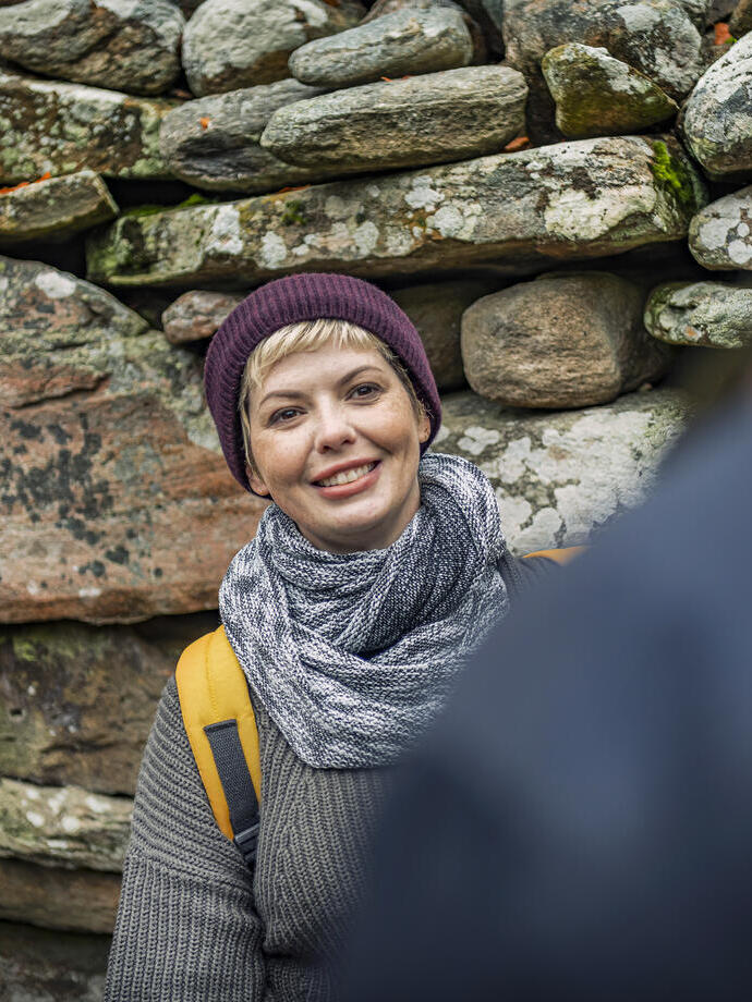 Frau mit Hut und Schal posiert vor einer Steinmauer