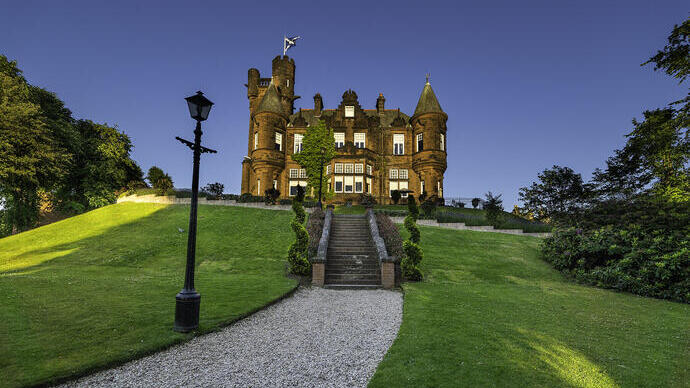 Grand château en pierre sur une colline verte avec un ciel bleu clair en arrière-plan.