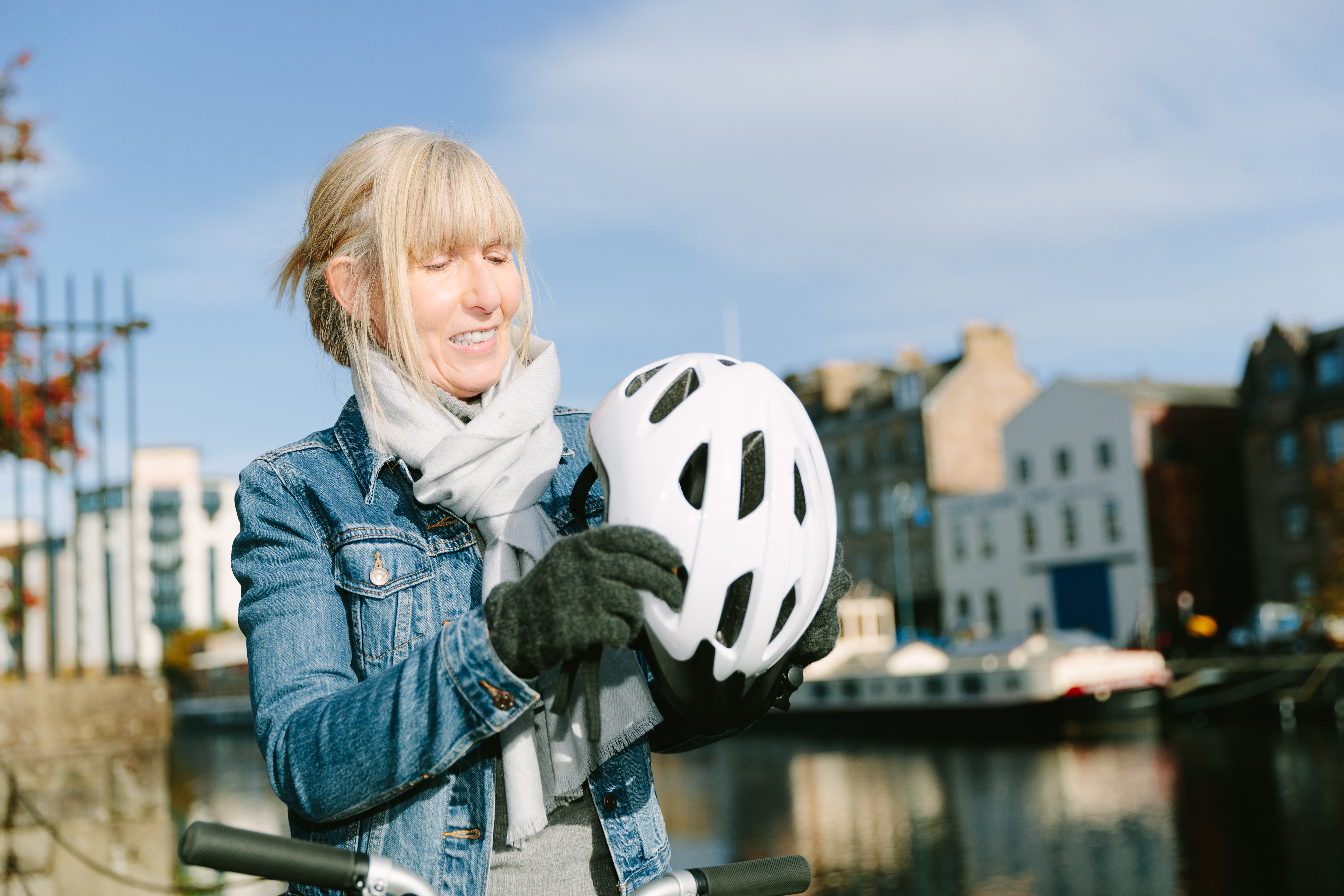 A woman putting on her bike helmet by the riverfront on a sunny day